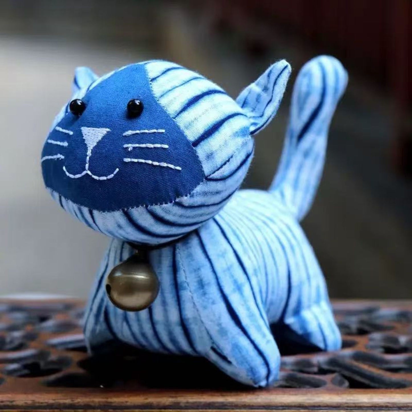 Close-up of a handcrafted indigo tie-dye plush cat with a small brass bell and intricate white stitching.