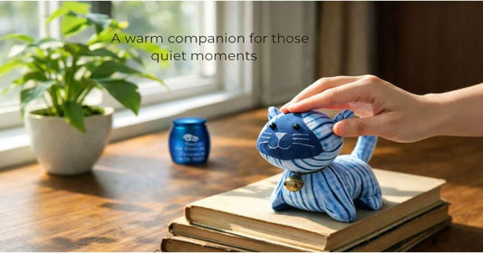 A hand petting a shibori blue tie-dye plush cat on a wooden window sill, serving as a warm companion for pet loss healing.