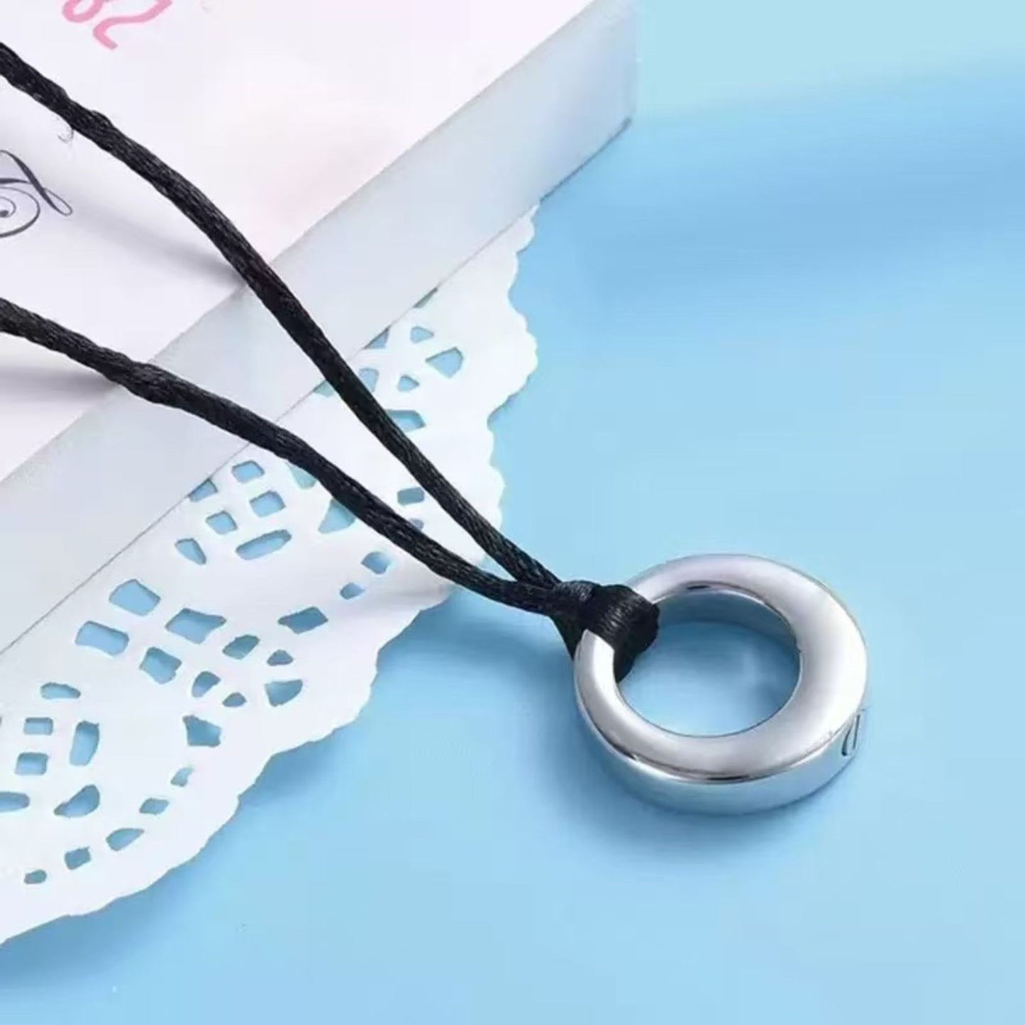 Close-up of silver hollow circle urn pendant on adjustable black cord necklace