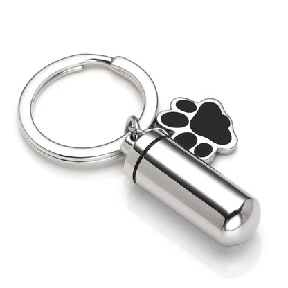 Silver stainless steel pet memorial ashes keychain urn with black paw charm and removable inner capsule on white background