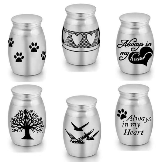 Stainless steel mini pet keepsake urn design options including paw prints, “Always in My Heart,” hearts band, tree, and birds