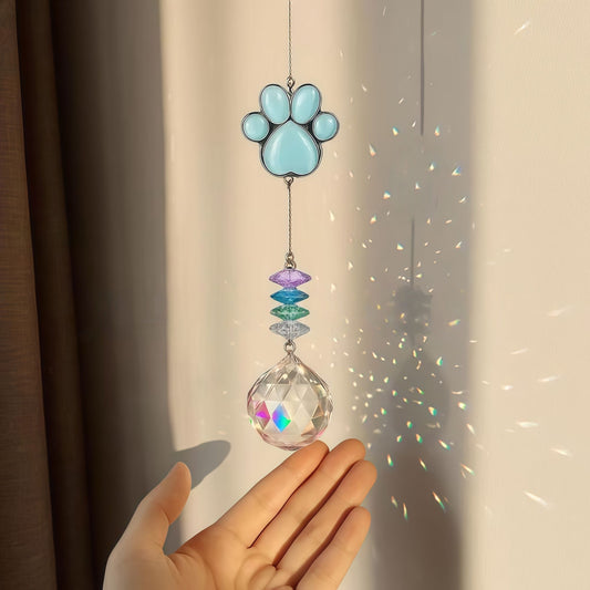 Blue paw suncatcher hanging in sunlight, rainbow prism reflections on wall