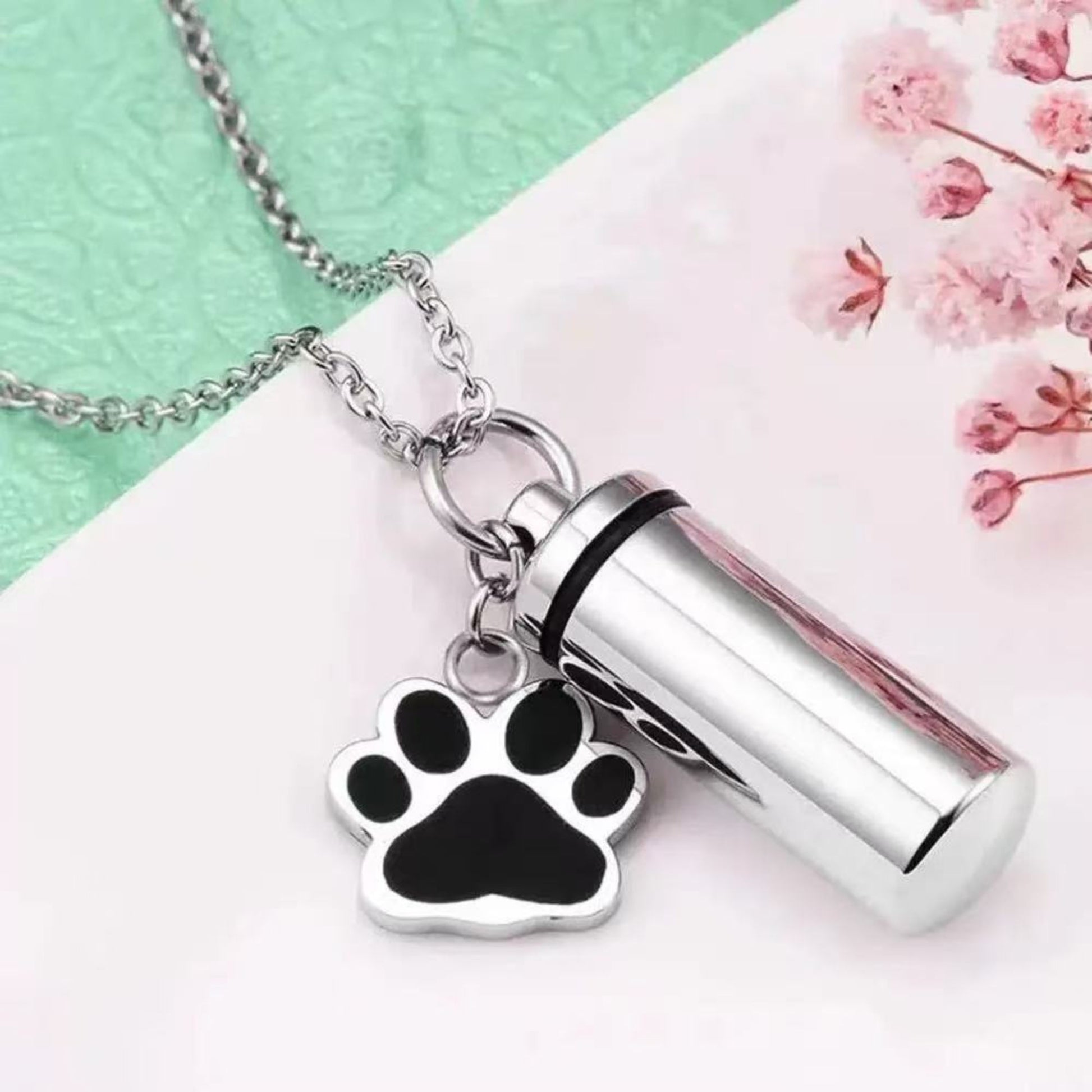 Close-up of silver pet memorial keepsake urn keychain with paw charm, opened screw-top design, and inner capsule insert