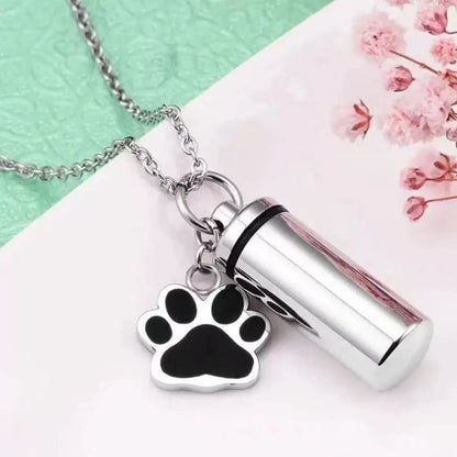 Close-up of silver pet memorial keepsake urn keychain with paw charm, opened screw-top design, and inner capsule insert
