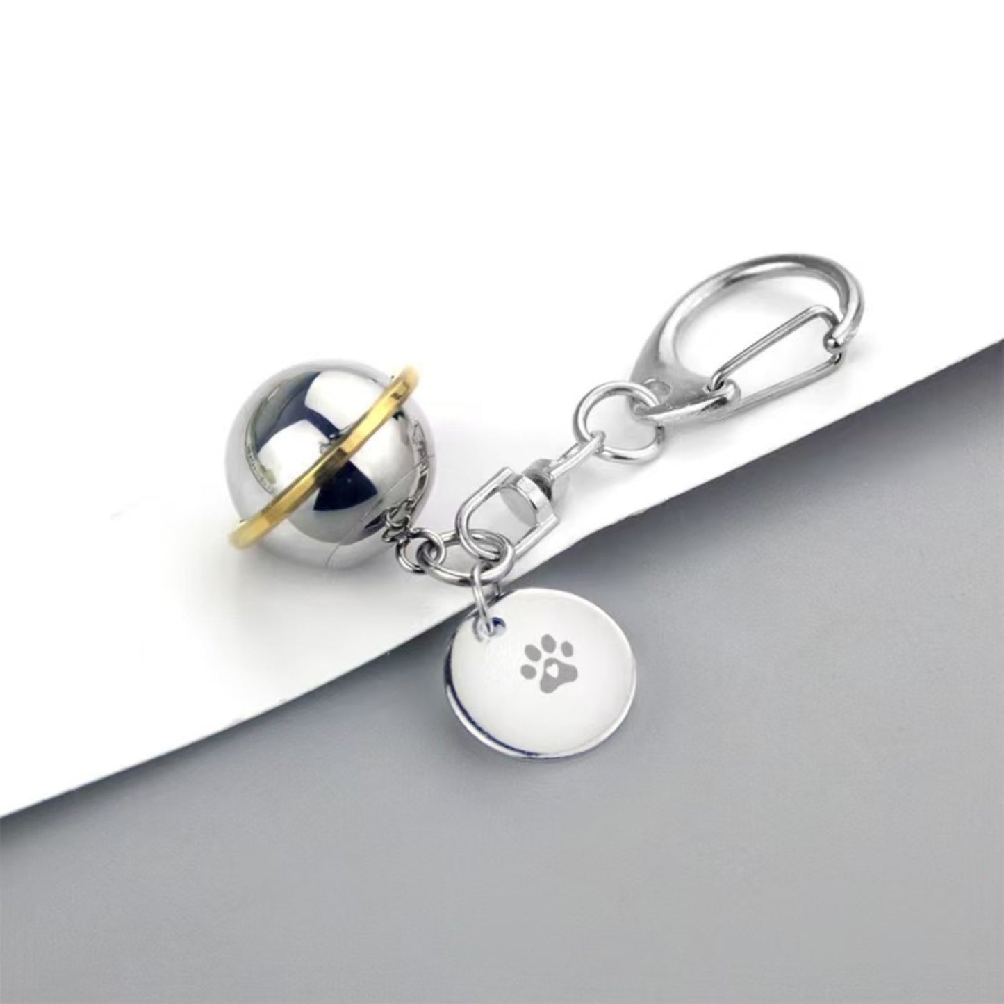 Side view of round planet memorial urn keychain with paw charm on a gray surface