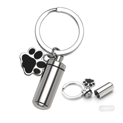 Close-up of silver pet memorial keepsake urn keychain with paw charm, opened screw-top design, and inner capsule insert