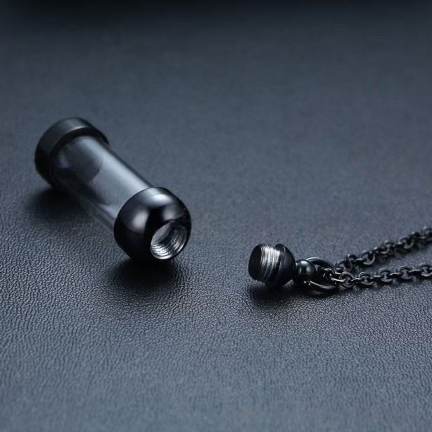 Close-up of opened black memorial tube pendant showing screw cap and inner chamber