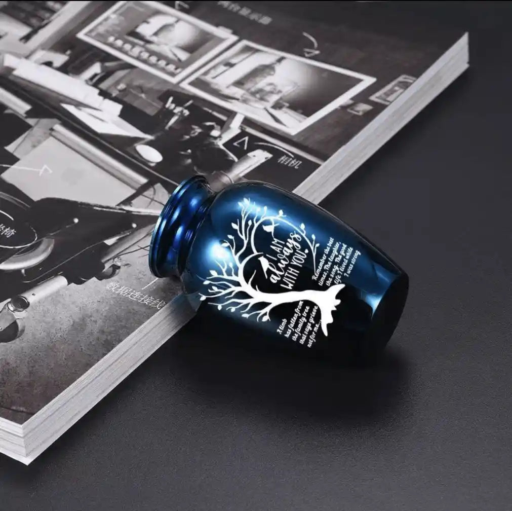 Close-up of a blue pet memorial urn with engraved tree design and remembrance quote, placed on a magazine for product detail display.