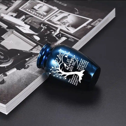 Close-up of a blue pet memorial urn with engraved tree design and remembrance quote, placed on a magazine for product detail display.