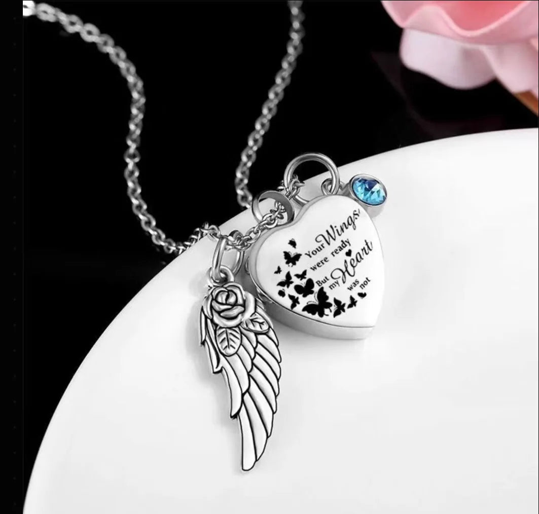 An angel wings heart pet urn necklace sitting elegantly next to a rose flower.