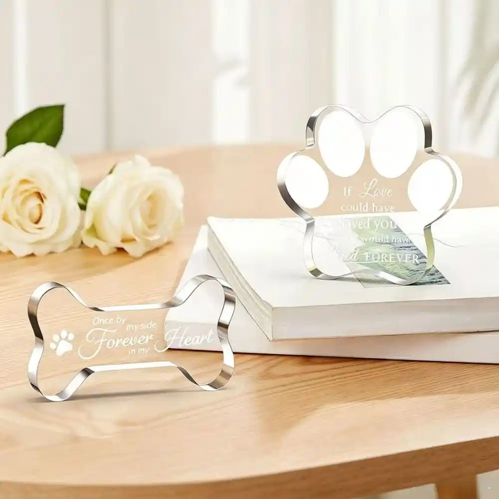 Freestanding acrylic pet memorial plaques in paw and bone shapes on a table.
