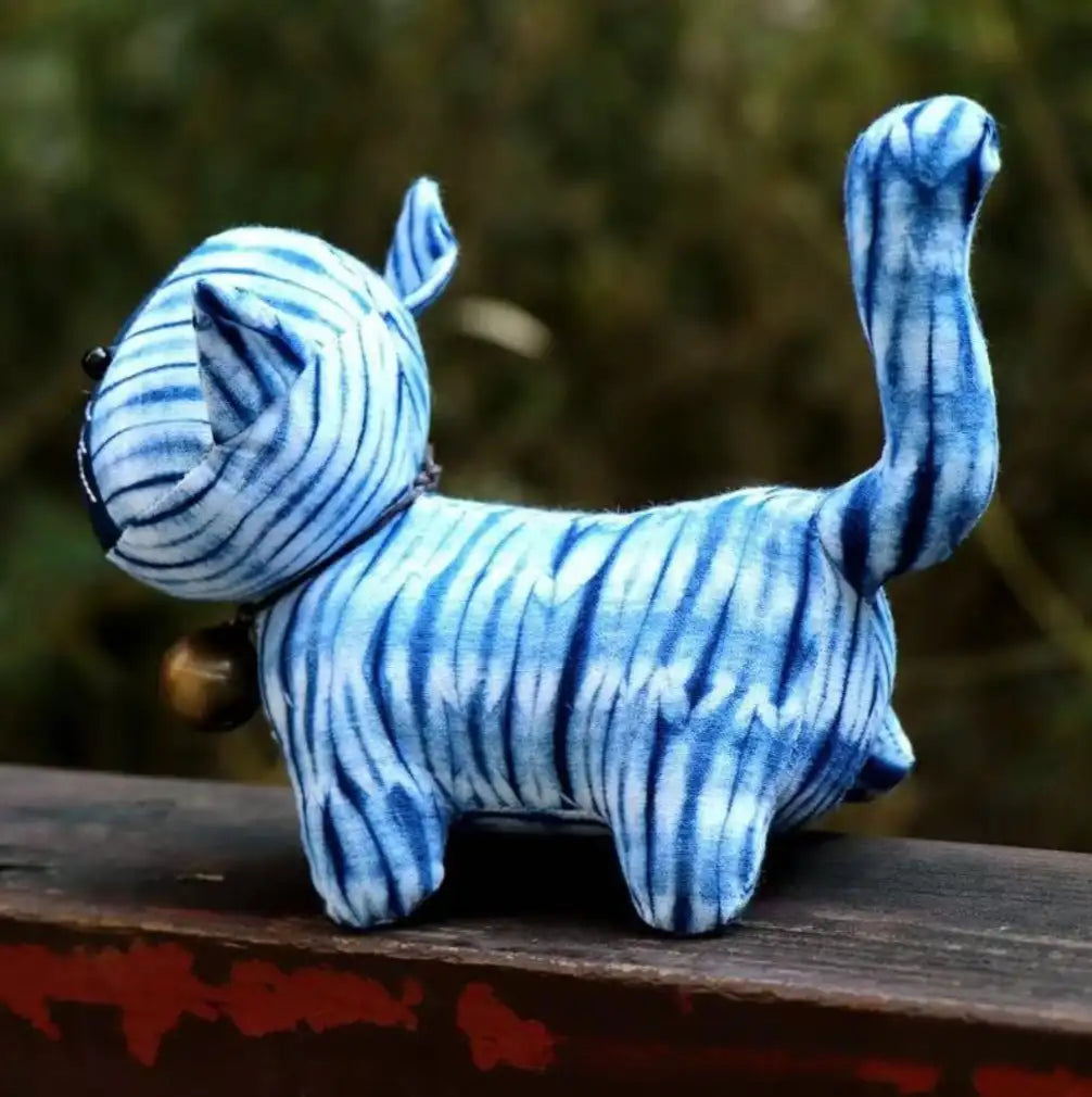 Side view of the handcrafted blue traditional Chinese tie-dye fabric plush cat with an upright tail sitting outdoors.