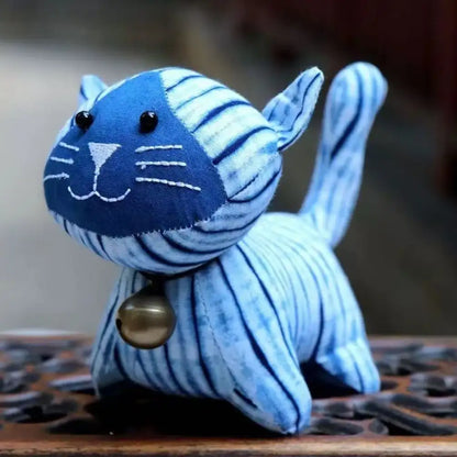 Close-up of a handcrafted indigo tie-dye plush cat with a small brass bell and intricate white stitching.