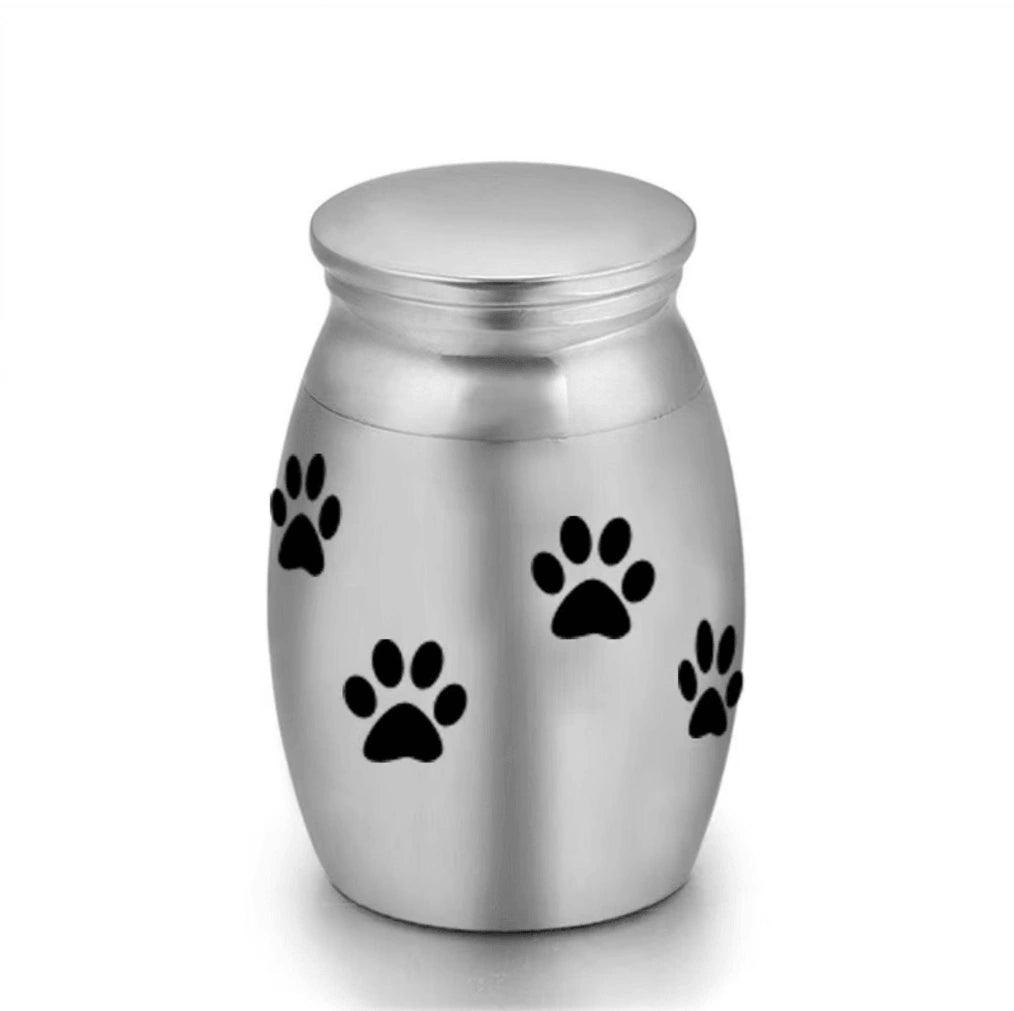 Isolated front view of the ultra-miniature 316L stainless steel pet keepsake urn featuring black laser-etched paw prints.