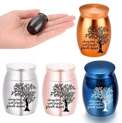 A selection of miniature pocket pet urns and memorials with a black capsule held in a hand for scale.