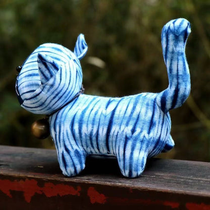 Side view of a soft blue indigo tie-dye memorial cat plush on a dark wooden surface.